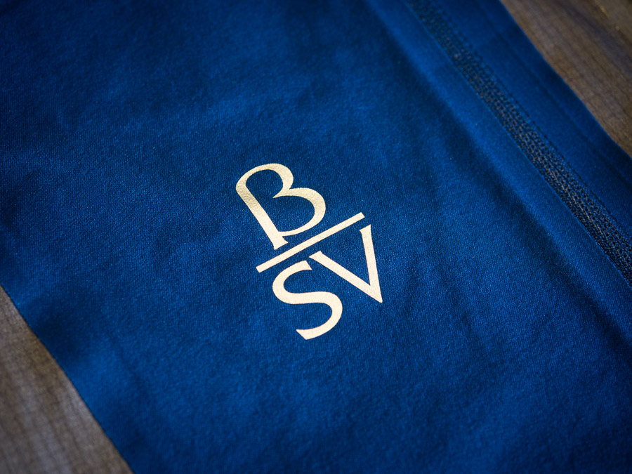 Photo of embossed white reflective text on a dark blue textile. The text reads: greek letter Beta, with an underline, and below it the letters S and V.