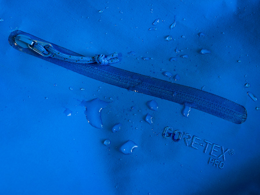 Photo of the left sleeve of the jacket. This shows the left bicep pocket zipper. The embroidered and color-matched Gore-Tex Pro logo. And some water droplets sitting on the surface of the jacket for visual appeal.