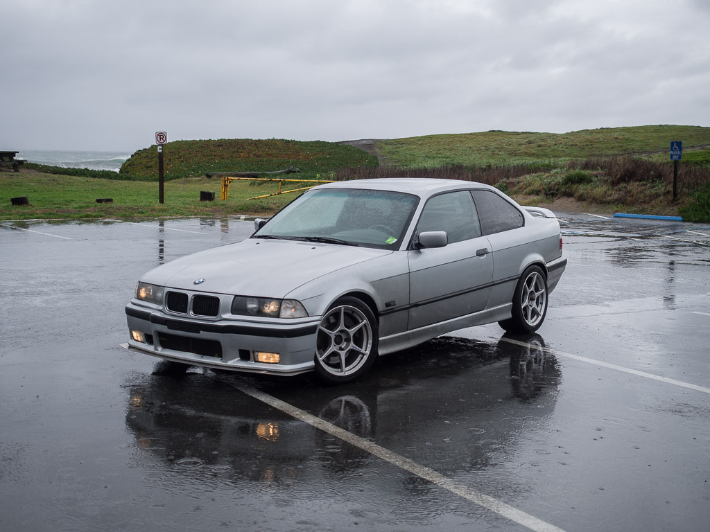 1996 BMW 328is idling in a beach parking lot in the rain.
